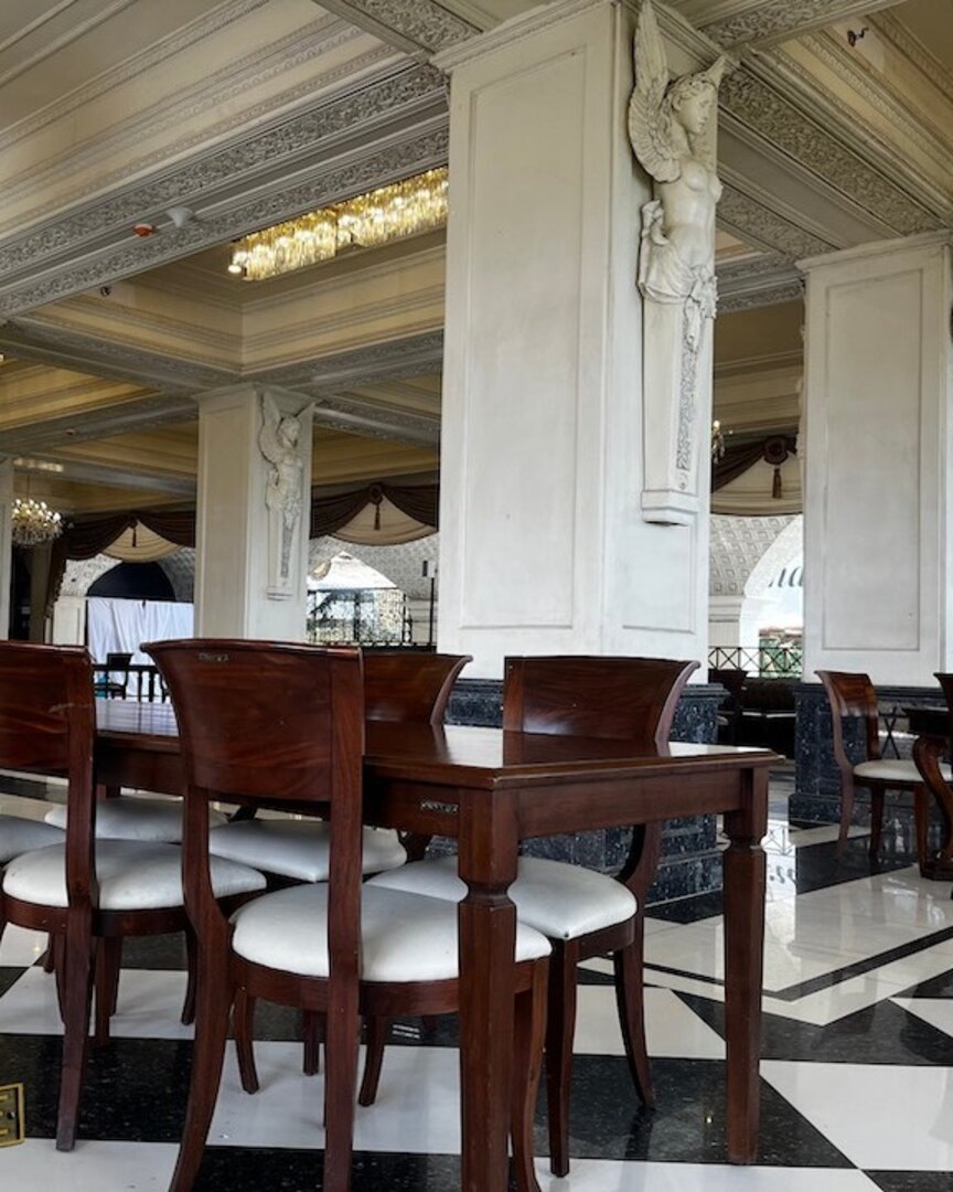 Solid wood dining tables and chairs with white upholstered seats in a grand hotel restaurant